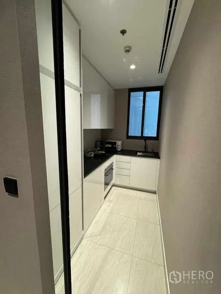 Condominium for rent in Bang Rak, Bangkok - Sleek galley kitchen with white cabinetry, black countertop and a window