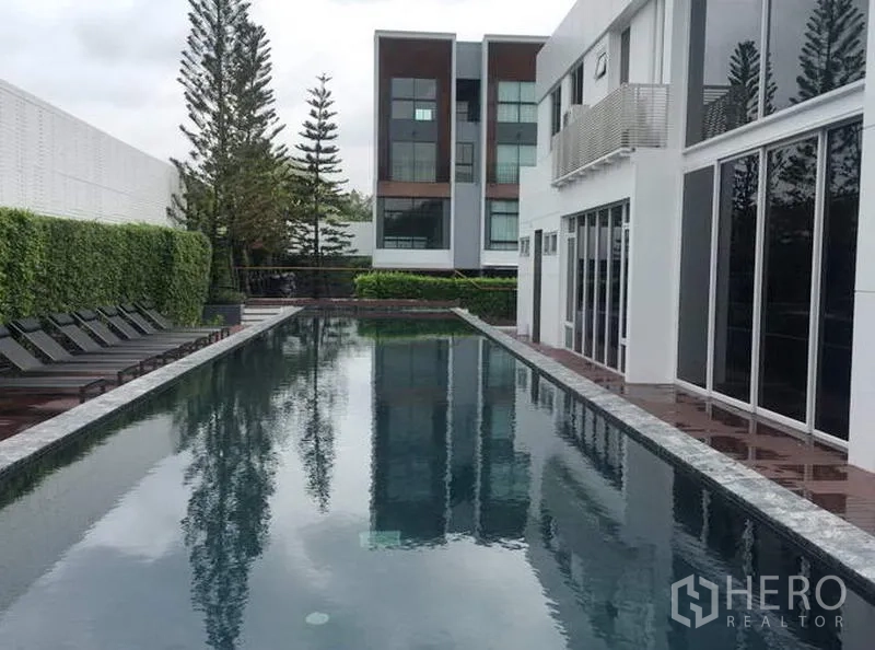 Townhouse for rent in Suan Luang, Bangkok - Long lap swimming pool with sun loungers and a glass‑fronted clubhouse at the end.