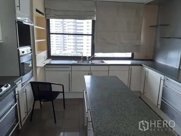 Condominium for rent in Khlong Toei, Bangkok - Bright U-shaped kitchen with granite island, white cabinets and a large window with city view in Khlong Toei, Bangkok.