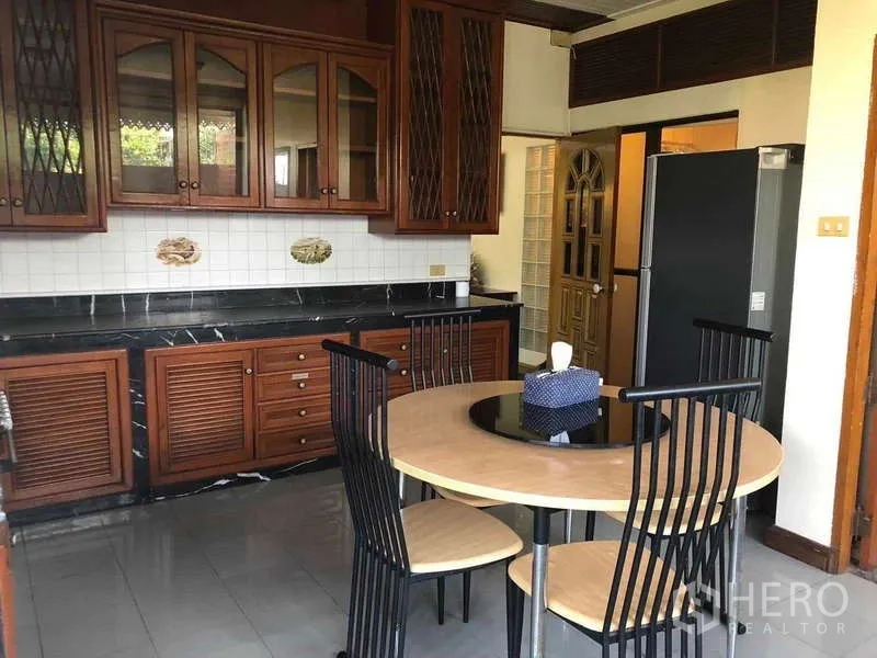 联排别墅 出租在Khlong Toei, Bangkok - 封闭式厨房，木质橱柜、黑色台面与圆形餐桌