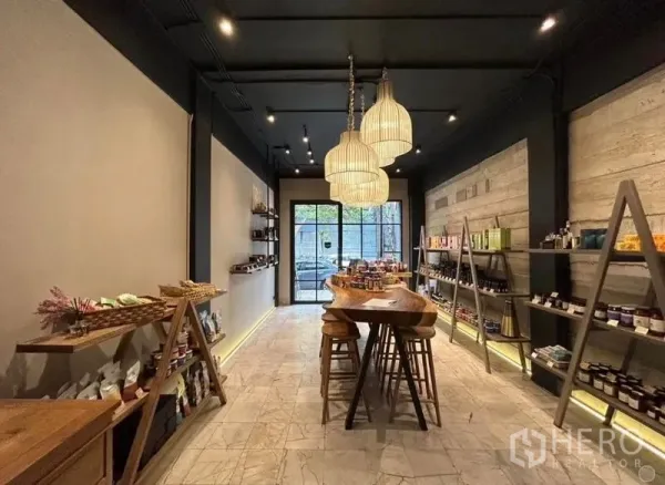 零售空间 出租在Bang Rak, Bangkok - 温暖灯光的零售店内景，木质展示台、吊灯、开放式货架与玻璃门面。