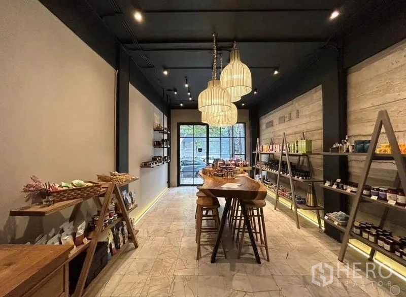 零售空间 出租在Bang Rak, Bangkok - 温暖灯光的零售店内景，木质展示台、吊灯、开放式货架与玻璃门面。