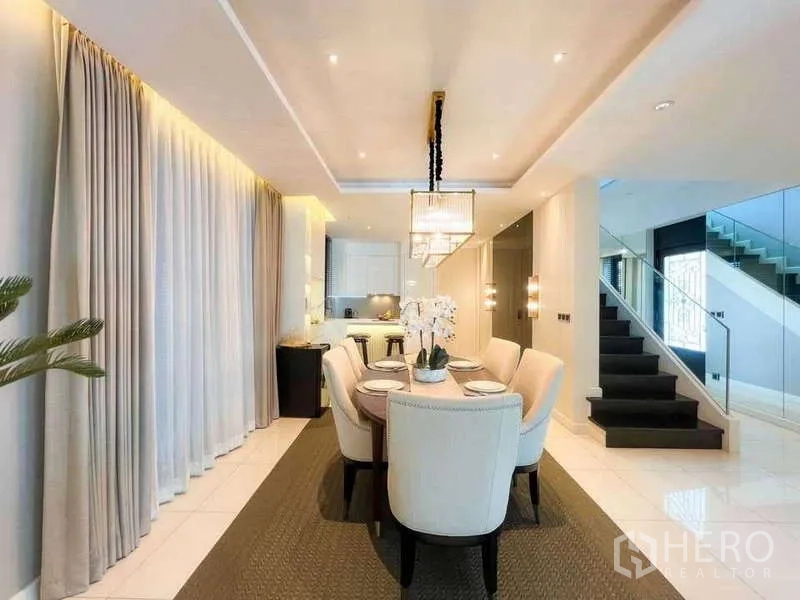 Detached House for sale in Bang Lamung, Chon Buri - Bright dining room with six‑seat table, pendant lights, open kitchen and glass‑railed staircase.