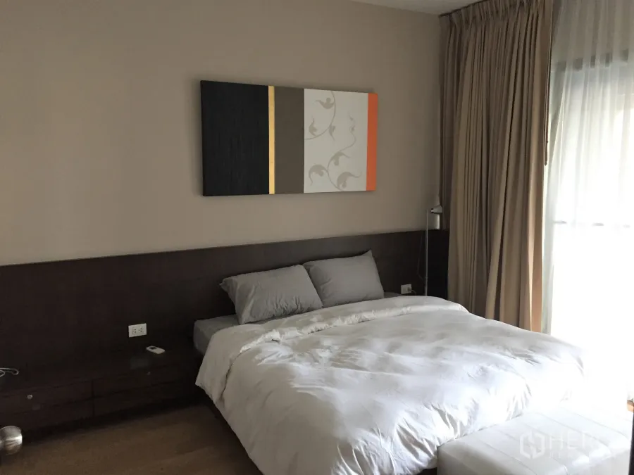 公寓 出租在Watthana, Bangkok - 主卧配深色木质床头、装饰画与落地窗帘，光线柔和的曼谷瓦他那区公寓卧室。
