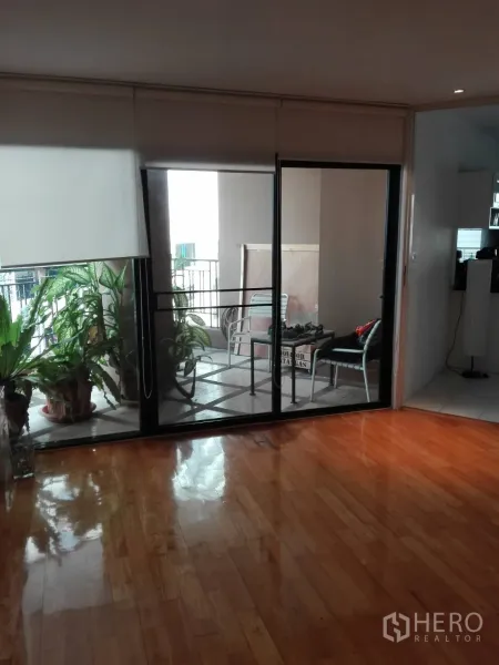 Condominium for rent in Khlong Toei, Bangkok - Sliding glass doors to a covered balcony with potted plants and outdoor seating.