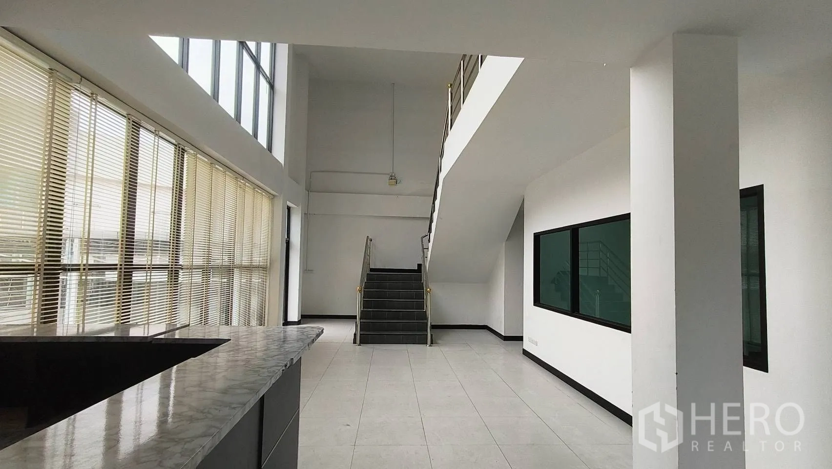 办公空间 出租在Khlong Toei, Bangkok - 挑高大厅，石纹接待台、楼梯和百叶窗。