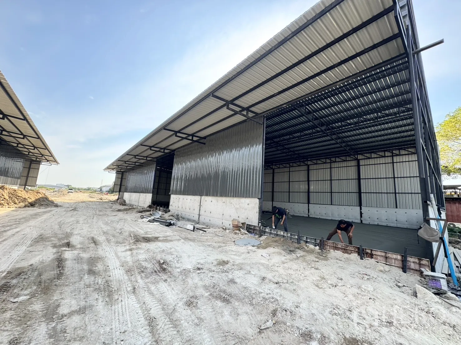 Warehouse for rent in Lam Luk Ka, Pathum Thani - External view of twin warehouses with wide canopies and freshly poured flooring.
