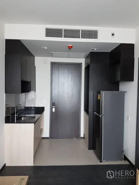 公寓 出租或出售在Watthana, Bangkok - 紧凑现代厨房，黑色石材台面、水槽、橱柜及冰箱，靠近入户门。
