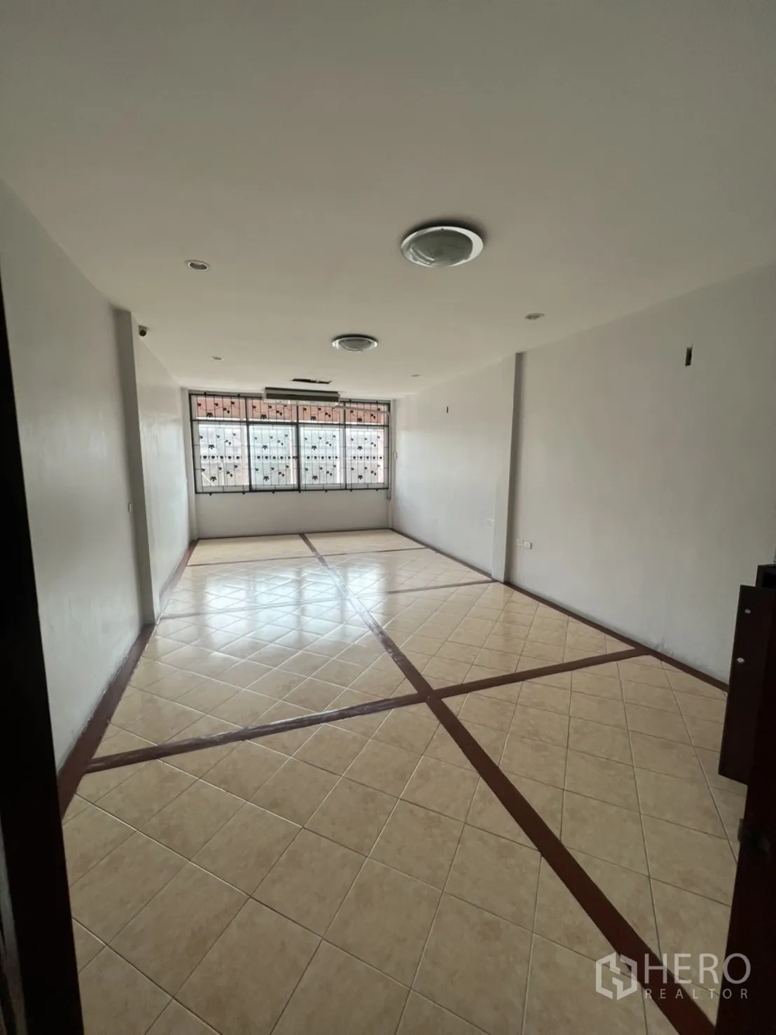 Shophouse for rent in Khlong Toei, Bangkok - Long open-plan room with patterned floor tiles and a wide end window.