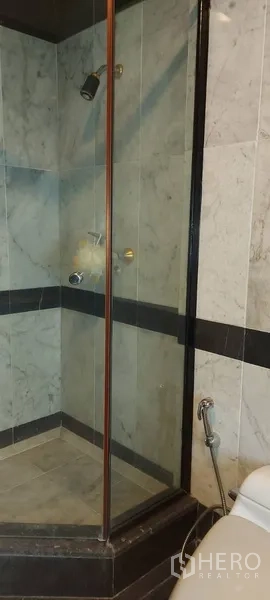 Condominium for rent in Sathon, Bangkok - Bathroom with a glass-enclosed shower and marble wall tiles.