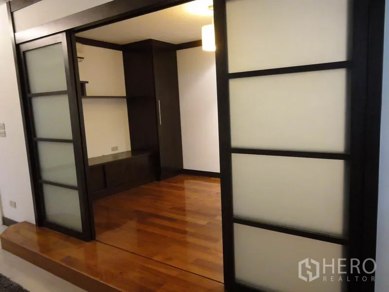Condominium for rent in Watthana, Bangkok - Room with dark-framed sliding doors, wooden floor and shelving.