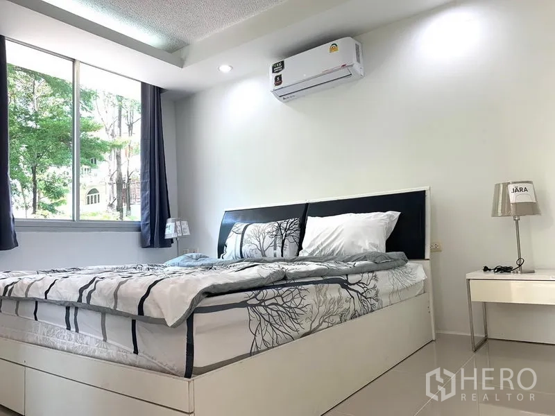 Condominium for rent or sale in Khlong Toei, Bangkok - Sunny bedroom with large window, curtains, air conditioner and matching bedside tables.