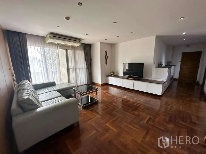 公寓 出租在Watthana, Bangkok - 开放式客厅，L 型沙发、电视柜与落地窗帘。