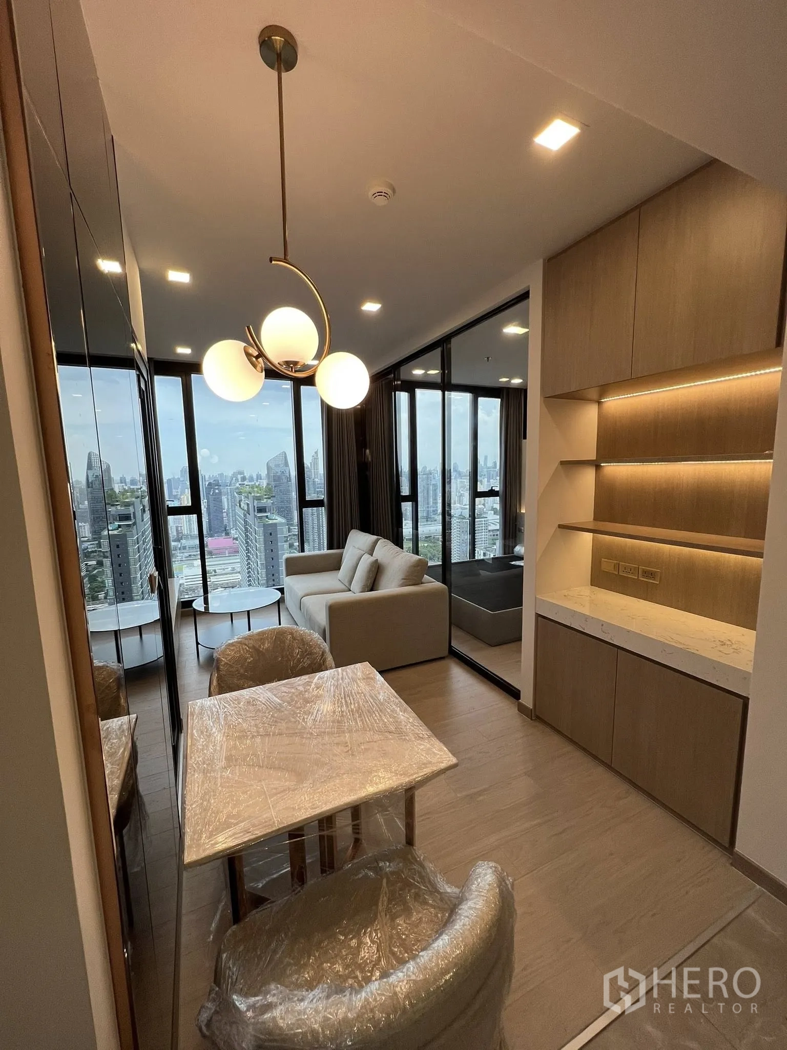 คอนโด for rent in Huai Khwang, Bangkok - โซนรับประทานอาหารและนั่งเล่นแบบเปิด พร้อมโคมไฟแขวน เตียงหลังบานกระจก มองเห็นวิวสกายไลน์