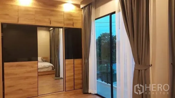 Detached House for sale in Samut Prakan - Master bedroom with built-in wood wardrobes, mirror panels and sliding glass door to the balcony.