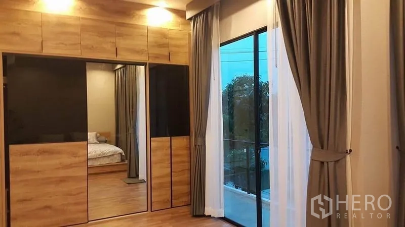 Detached House for sale in Samut Prakan - Master bedroom with built-in wood wardrobes, mirror panels and sliding glass door to the balcony.