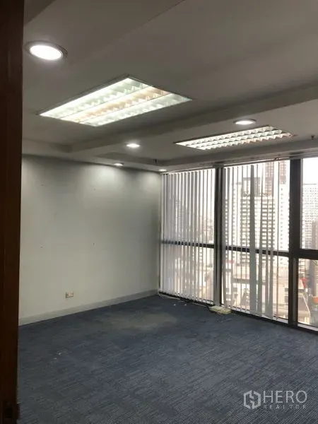 Office Space for rent - Bright open office area with large windows, vertical blinds, recessed lighting, and blue carpet tiles.