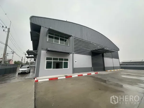 โรงงาน ให้เช่าในPathum Thani - ด้านหน้าโรงงานกรุเมทัลชีท ประตูม้วนสำหรับขนถ่ายสินค้าและพื้นที่จอดรถ
