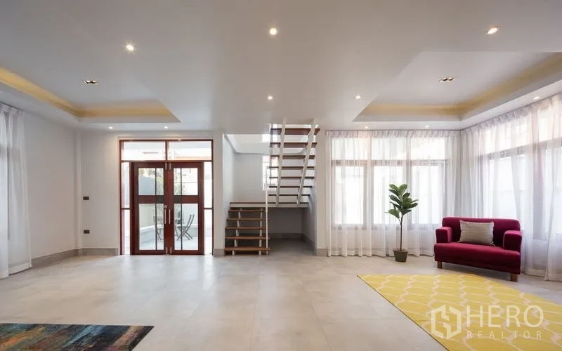 Detached House for sale in Chatuchak, Bangkok - Living area with floor-to-ceiling windows, open stairs and accent chair.