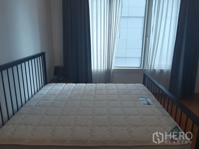 Condominium for rent in Khlong Toei, Bangkok - Master bedroom with large window, sheer and blackout curtains and a queen-size bed frame.