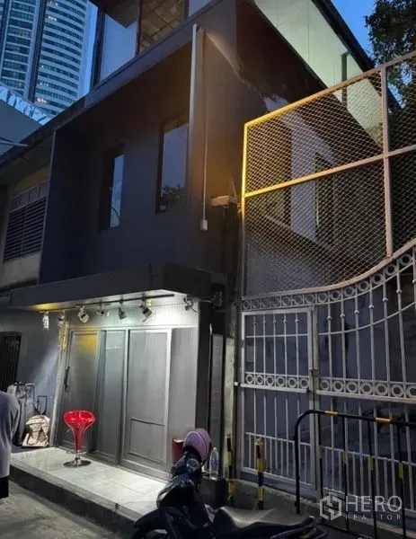 Retail Space for rent in Khlong Toei, Bangkok - Two-storey dark gray retail facade at dusk with gated side and spotlighted entrance.