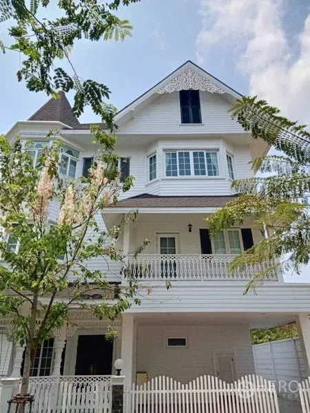 独立式住宅 出租在Bang Na, Bangkok - 三层白色独栋住宅，带阳台、山墙装饰与前庭树木。