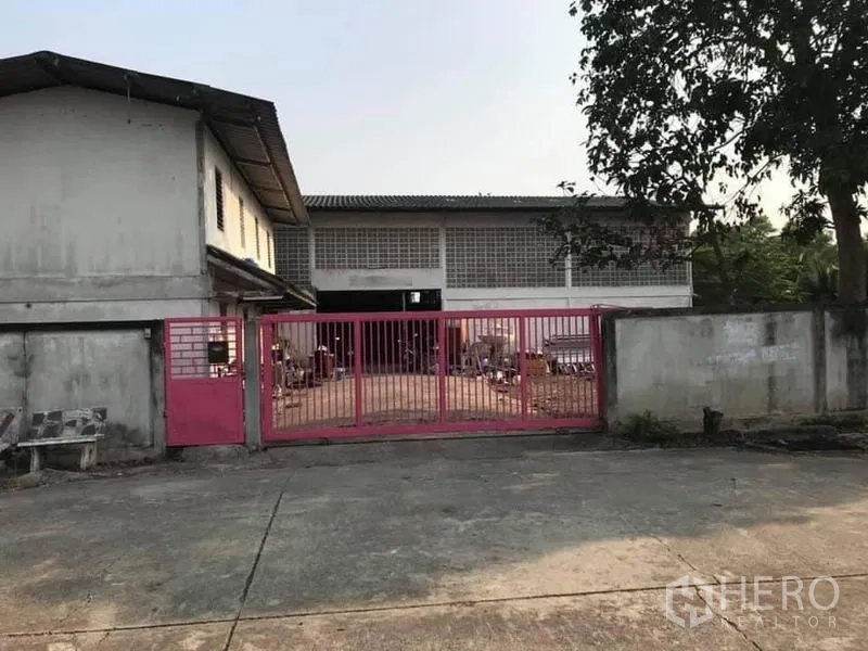 โรงงาน ขายในNong Chok, Bangkok - ทางเข้าโรงงานพร้อมประตูเหล็กสีชมพูและลานคอนกรีตในเขตหนองจอก กรุงเทพฯ