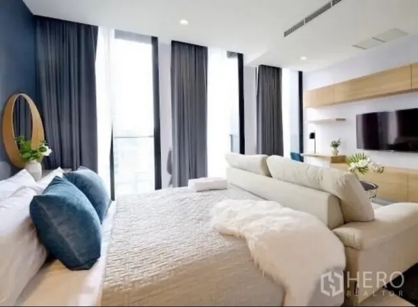 Condominium for rent in Pathum Wan, Bangkok - Airy bedroom with king bed, tall curtains, and city-view windows facing a built-in media wall.