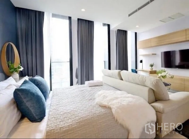 Condominium for rent in Pathum Wan, Bangkok - Airy bedroom with king bed, tall curtains, and city-view windows facing a built-in media wall.
