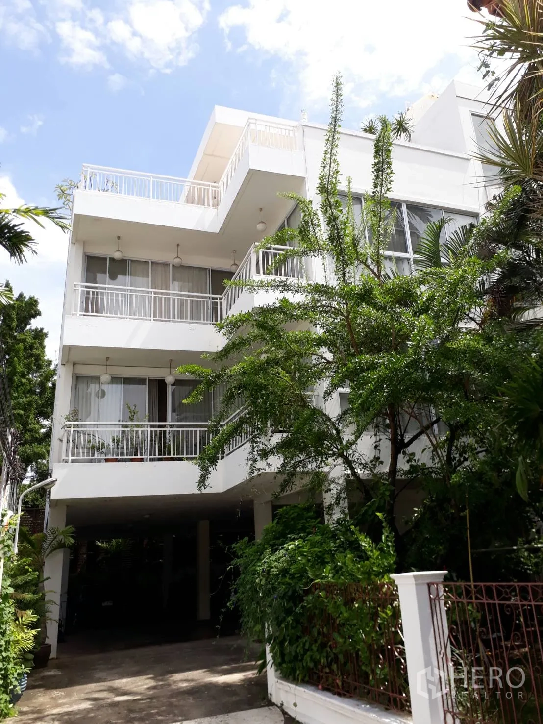 公寓 出租在Watthana, Bangkok - 白色低层公寓外观，带宽阔阳台与大窗户，绿植环绕并设有架空车位。