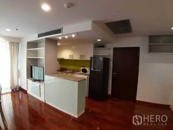 Condominium for rent or sale in Pathum Wan, Bangkok - Compact kitchen with a peninsula counter, open shelving and refrigerator in an open-plan layout.