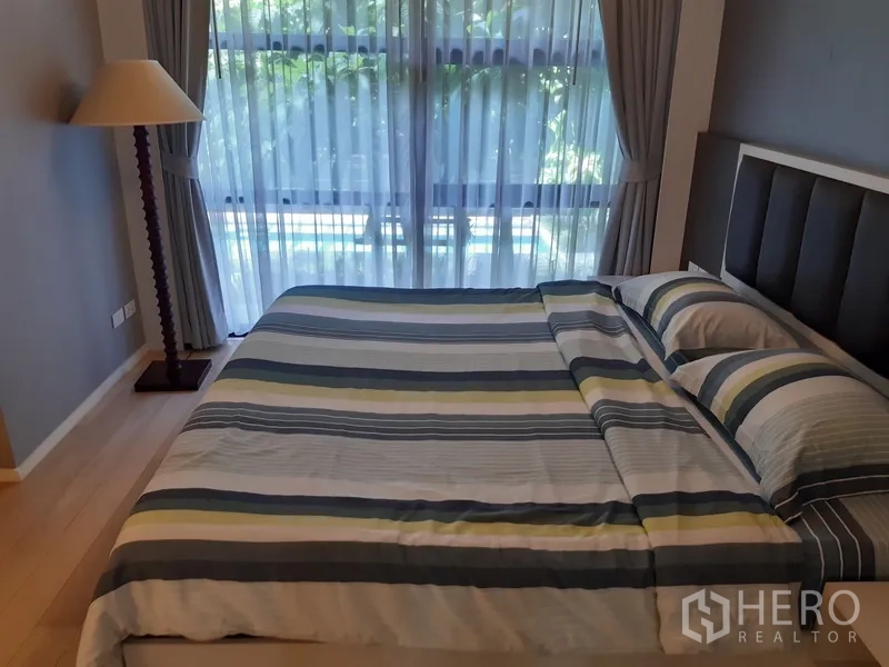 公寓 出租在Watthana, Bangkok - 明亮卧室配特大床与条纹床品，落地窗与窗帘外望绿景。
