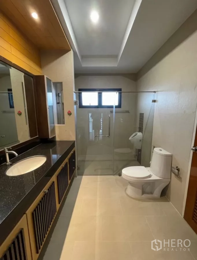 Detached House for rent in Chatuchak, Bangkok - Bathroom with long stone countertop, glass-enclosed shower and toilet.