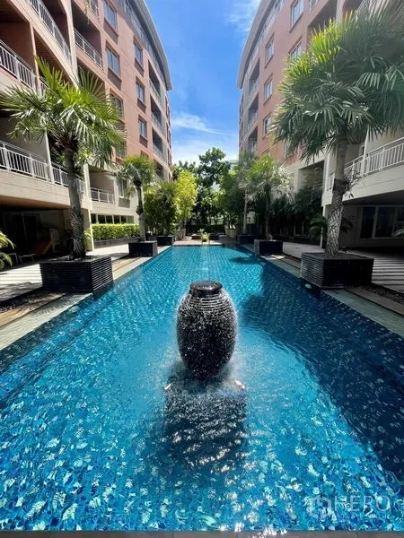 Condominium for rent - Resort-style long swimming pool with central water feature, palms and low-rise buildings.