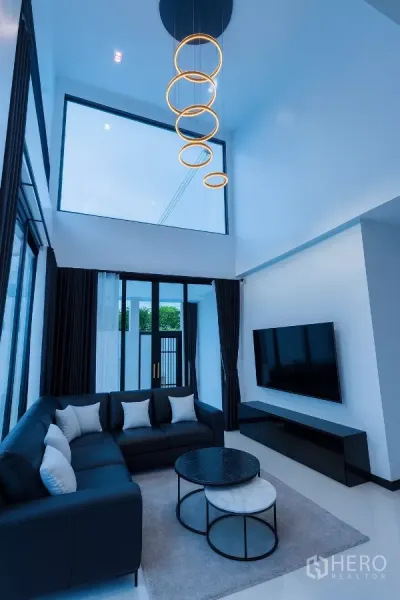 Detached House for rent in Wang Thonglang, Bangkok - Double-height living room with ring chandelier, L-shaped sofa, and floor-to-ceiling windows.