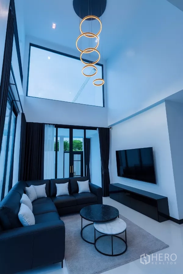 Detached House for rent in Wang Thonglang, Bangkok - Double-height living room with ring chandelier, L-shaped sofa, and floor-to-ceiling windows.
