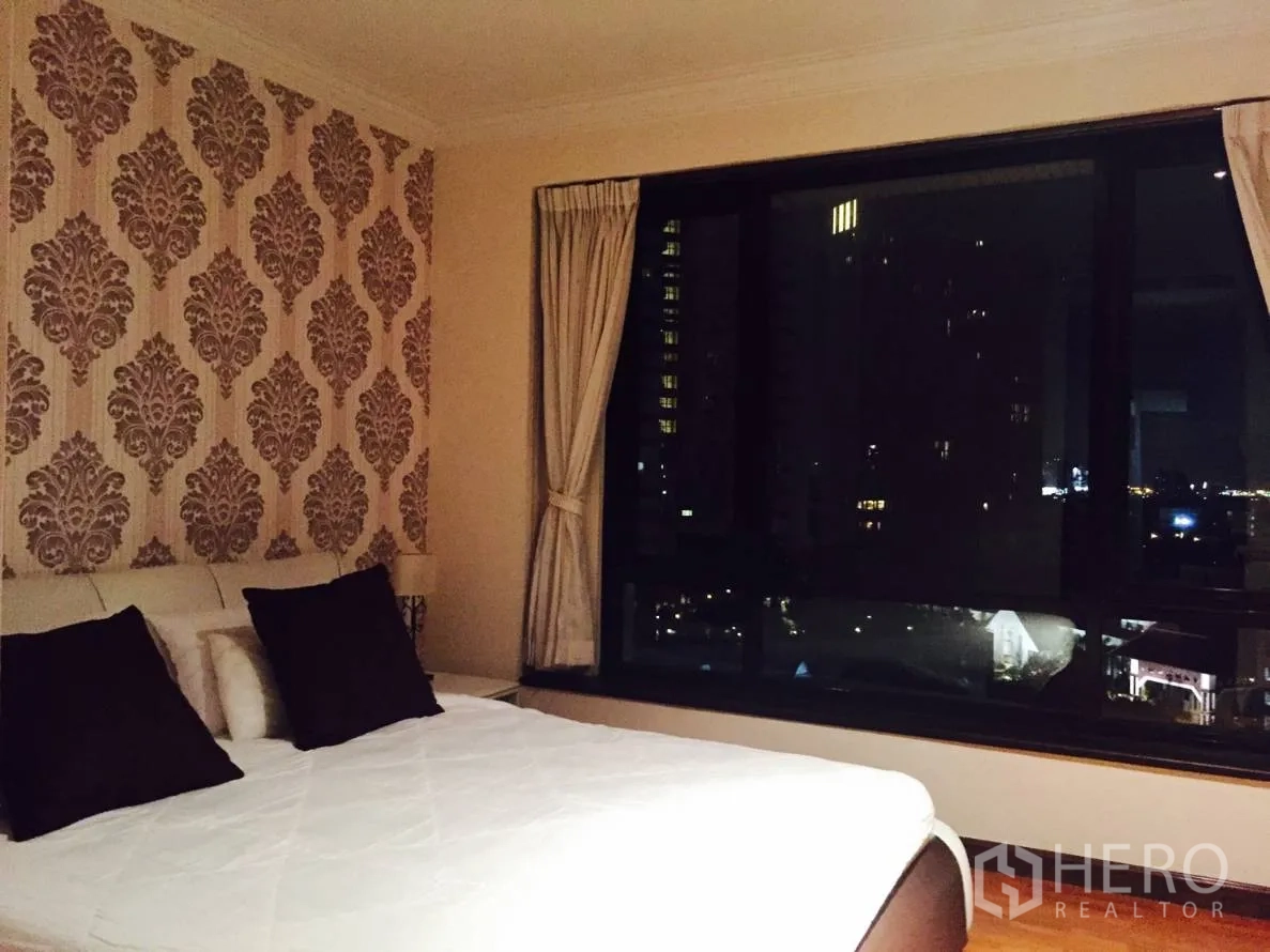 Condominium for rent in Sathon, Bangkok - Bedroom with patterned accent wall, large bed and a wide window framing the skyline at night.
