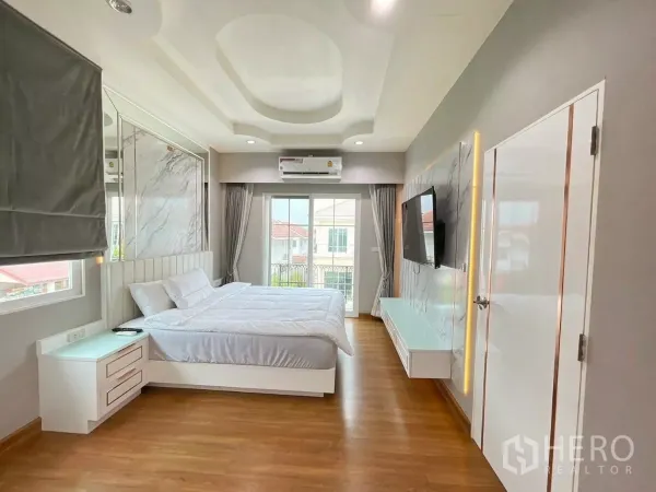 Detached House for rent in Bang Khen, Bangkok - Master bedroom with king bed, balcony doors, wall‑mounted TV and ceiling detail.