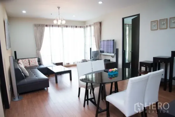Condominium for rent in Khlong Toei, Bangkok - Bright living and dining area with L-shaped leather sofa, glass table and floor-to-ceiling windows in a Sukhumvit condo.