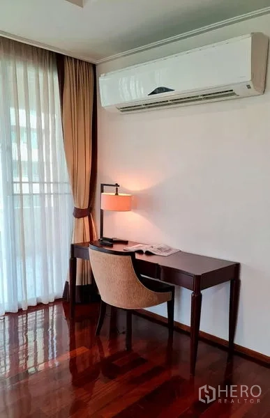 Apartment for rent in Khlong Toei, Bangkok - Bright work corner with desk and chair by full-height curtains and wall-mounted air conditioner.