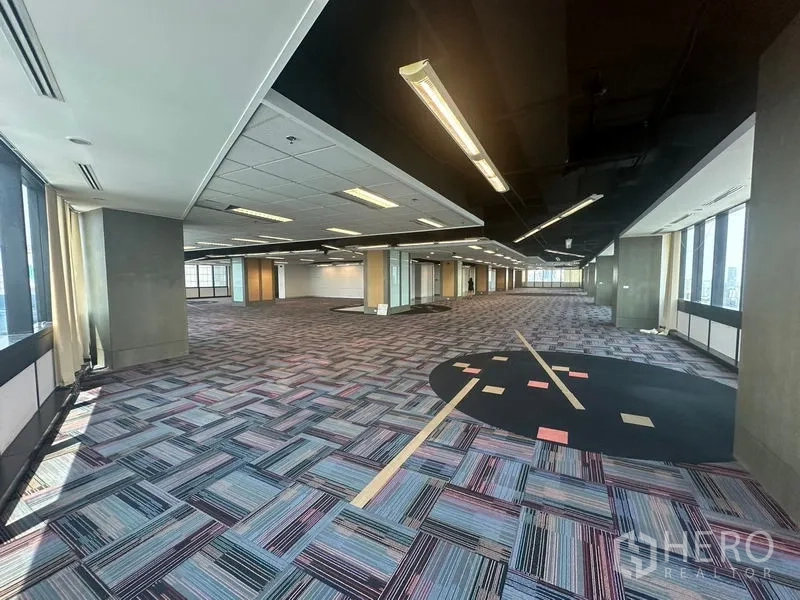 Office Space for rent in Khlong Toei, Bangkok - Expansive floor plate with circular carpet feature and exposed black ceiling.