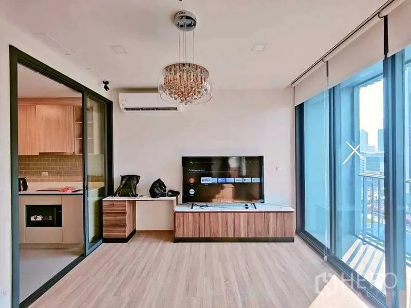 Condominium for rent in Ratchathewi, Bangkok - Living room with chandelier, TV console and glazing to a balcony view.