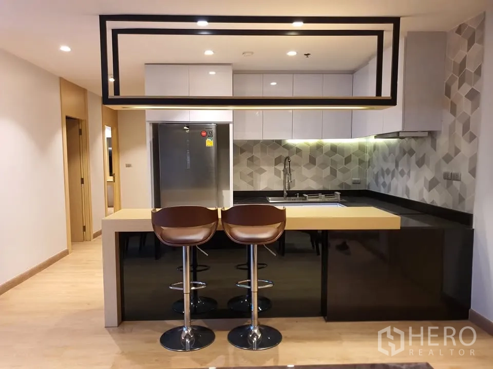 Condominium for rent in Watthana, Bangkok - Modern kitchen with island breakfast bar, suspended frame, fridge and geometric backsplash.