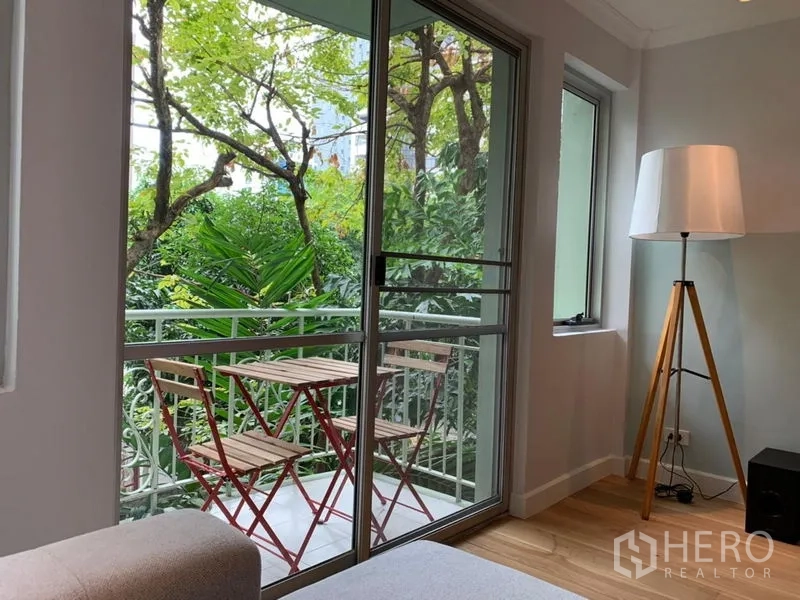 Condominium for sale in Watthana, Bangkok - Compact balcony with bistro table and chairs facing leafy trees.