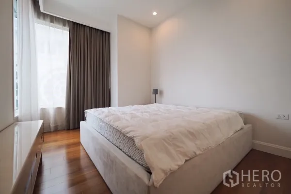 Condominium for rent in Pathum Wan, Bangkok - Primary bedroom with large bed, wood floors and floor-to-ceiling curtains.