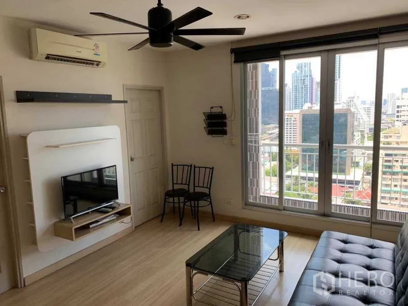 Condominium for rent in Bang Rak, Bangkok - Living room with sliding glass doors to a balcony, city views, sofa and TV unit.