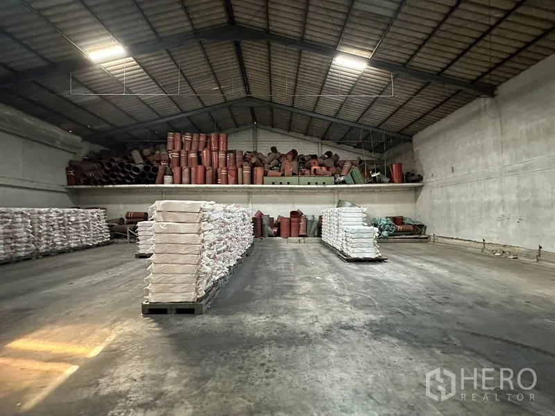 货栈 出租在Lat Krabang, Bangkok - 仓库内部空间宽敞，混凝土地面，高挑屋顶与夹层储物，物资堆放整齐。