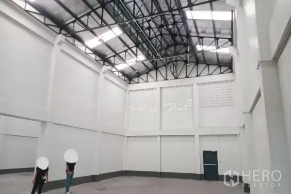 Warehouse for rent in Mueang Samut Sakhon, Samut Sakhon - Bright high-bay warehouse hall with steel truss roof, ventilation blocks and an emergency exit door.