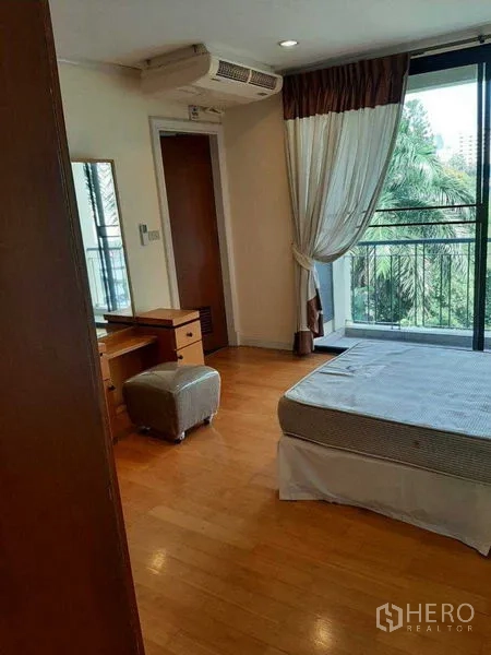 Apartment for rent in Watthana, Bangkok - Bedroom with balcony access, vanity table, air-conditioning, and leafy views.