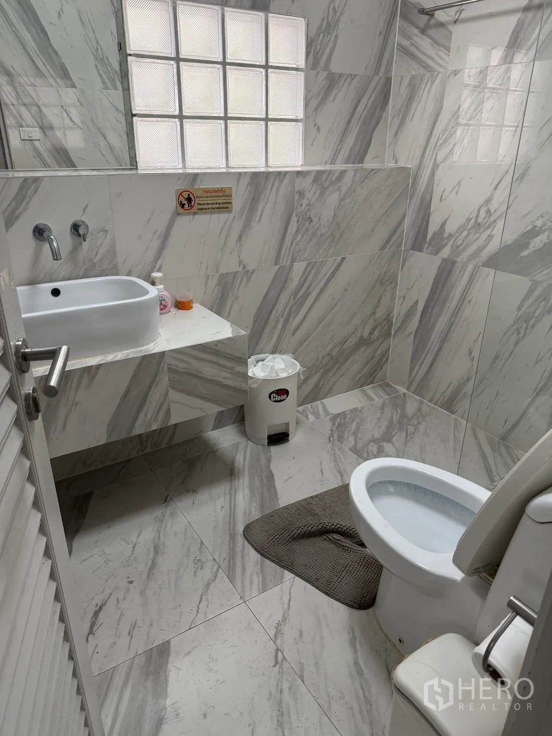Home Office for rent in Watthana, Bangkok - Bathroom finished with marble-effect tiles, a glass-block window, wall-mounted sink, and toilet.